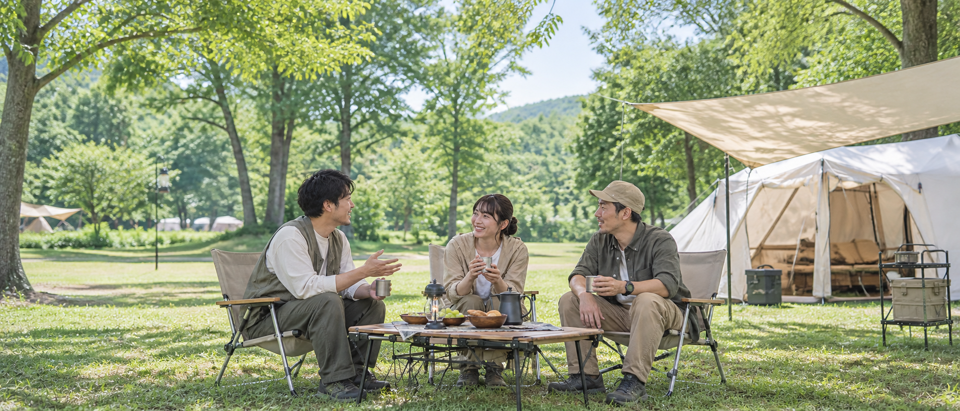明るい芝生サイトで、キャンプテーブルとローチェアを囲んで穏やかに話す3人のキャンパーのイメージ